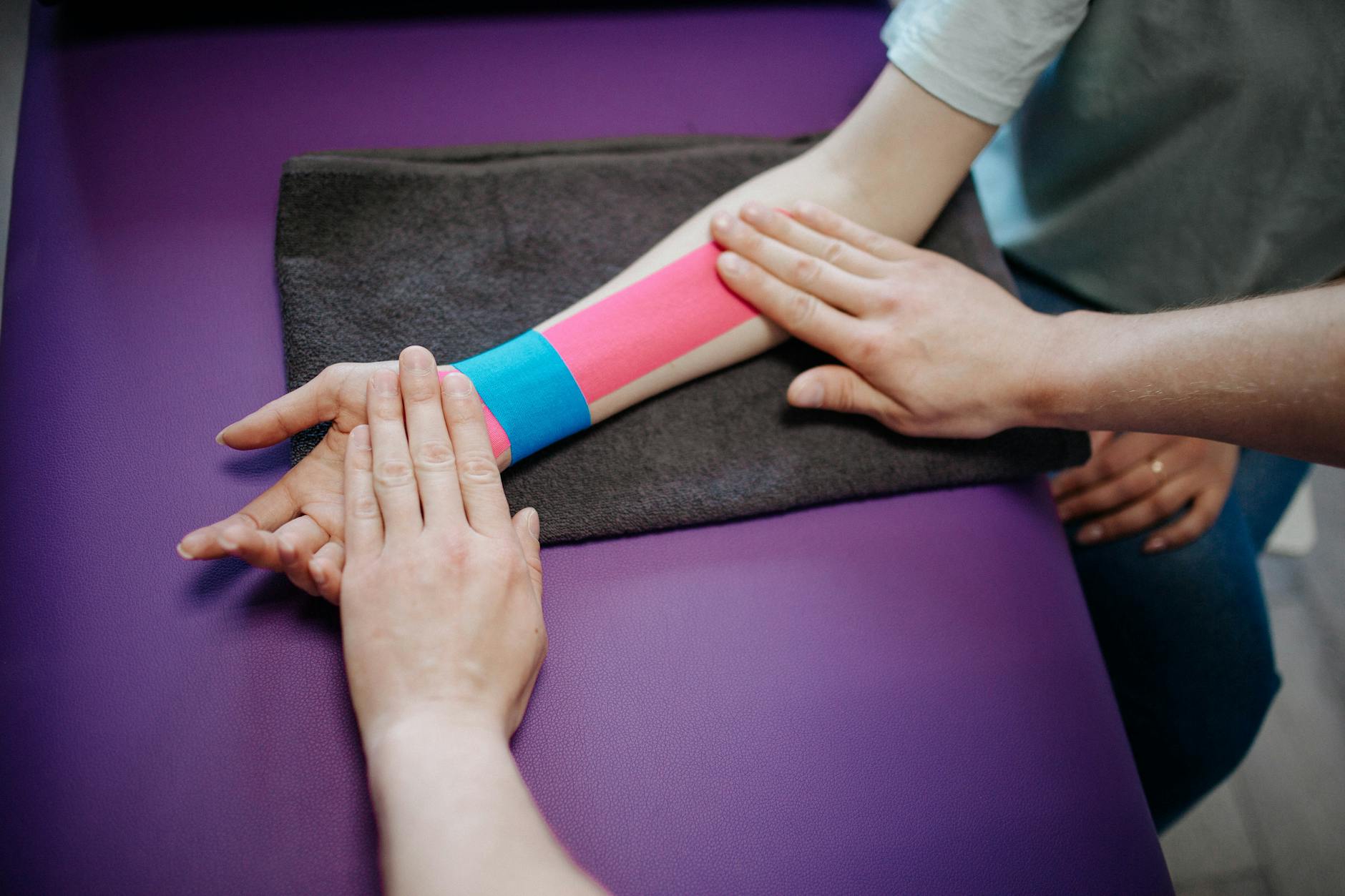 Fizjoterapeuta nakleja kolorowe tejpy kinezjologiczne na przedramię pacjenta
