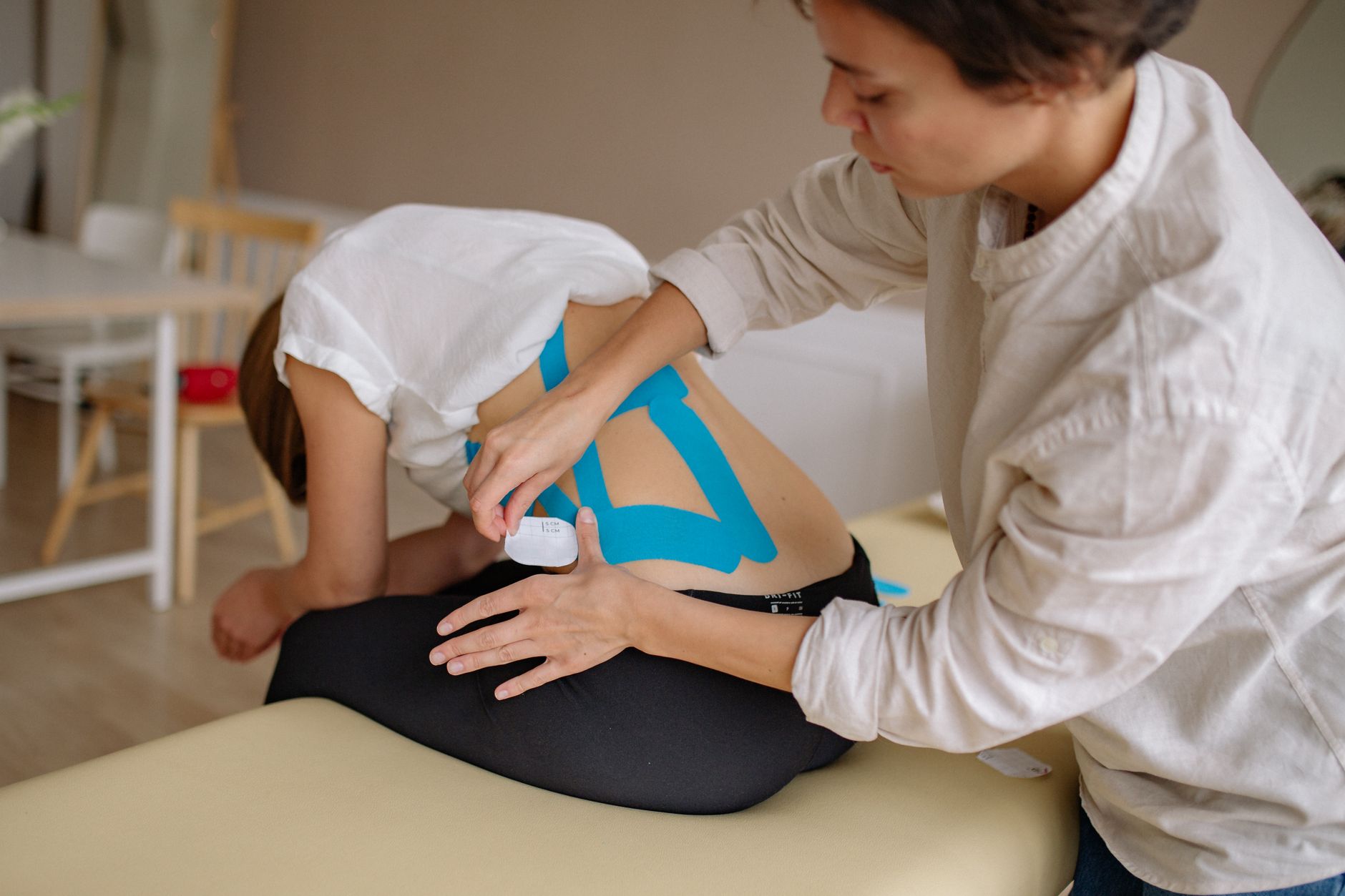Fizjoterapeuta nakleja niebieskie taśmy kinesio na plecy pacjenta